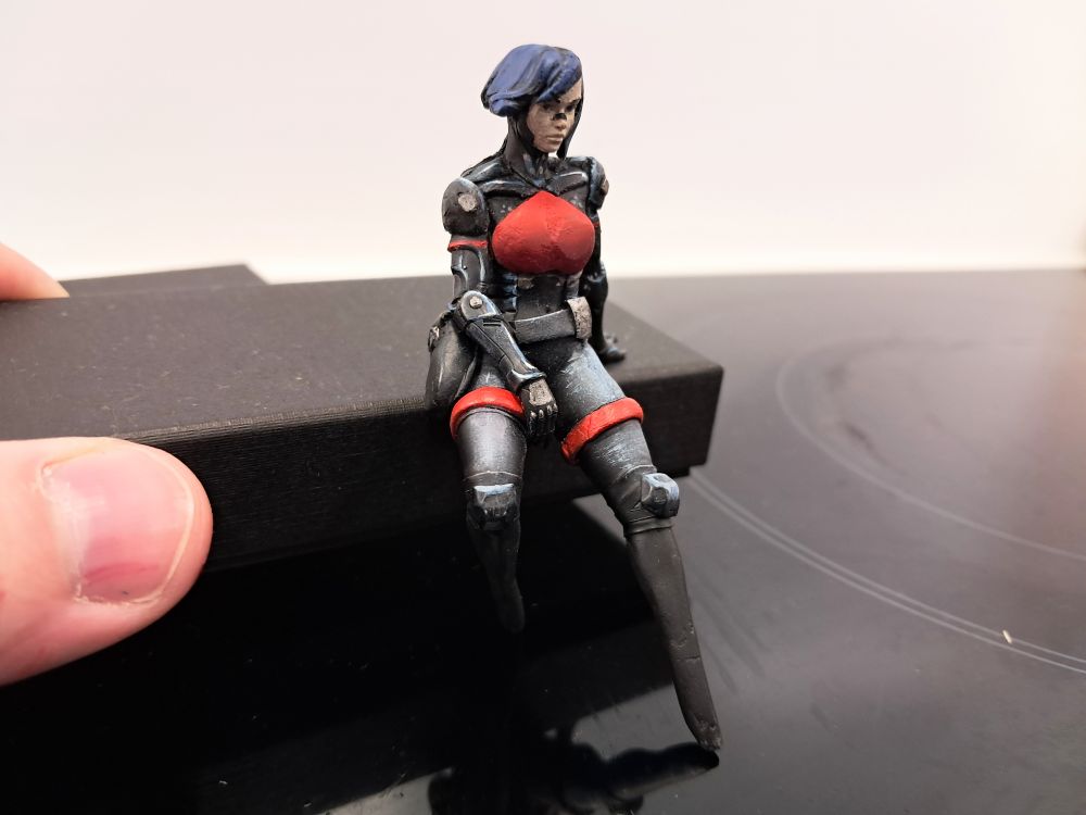 Photograph depicting a kitbashed "75mm" Elster miniature from Signalis. It's been extremely heavily customised from an entirely different mini to look as much like her as possible.
Specifically the legs and chest plate in these images were modelled from milliputt, and had serious problems with rough surfaces and irregular shapes on account of me doing it entirely with my fingers and without vaseline to prevent fingerprinting and adhesion to my fingers. They have now been sanded down with fine-grit sandpaper, cleaned and repainted to provide a much better finish. Details can now be painted on top to show the ties etc.
