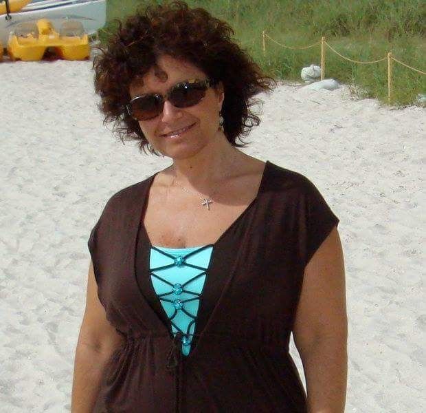 Woman with curly hair and sunglasses standing on a beach. Alive.