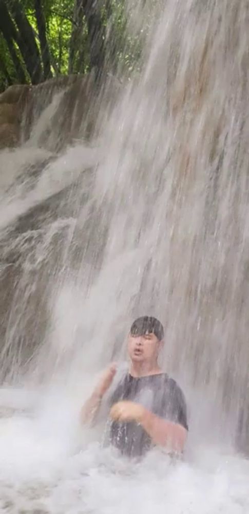 a man is standing under a waterfall with his head in the water