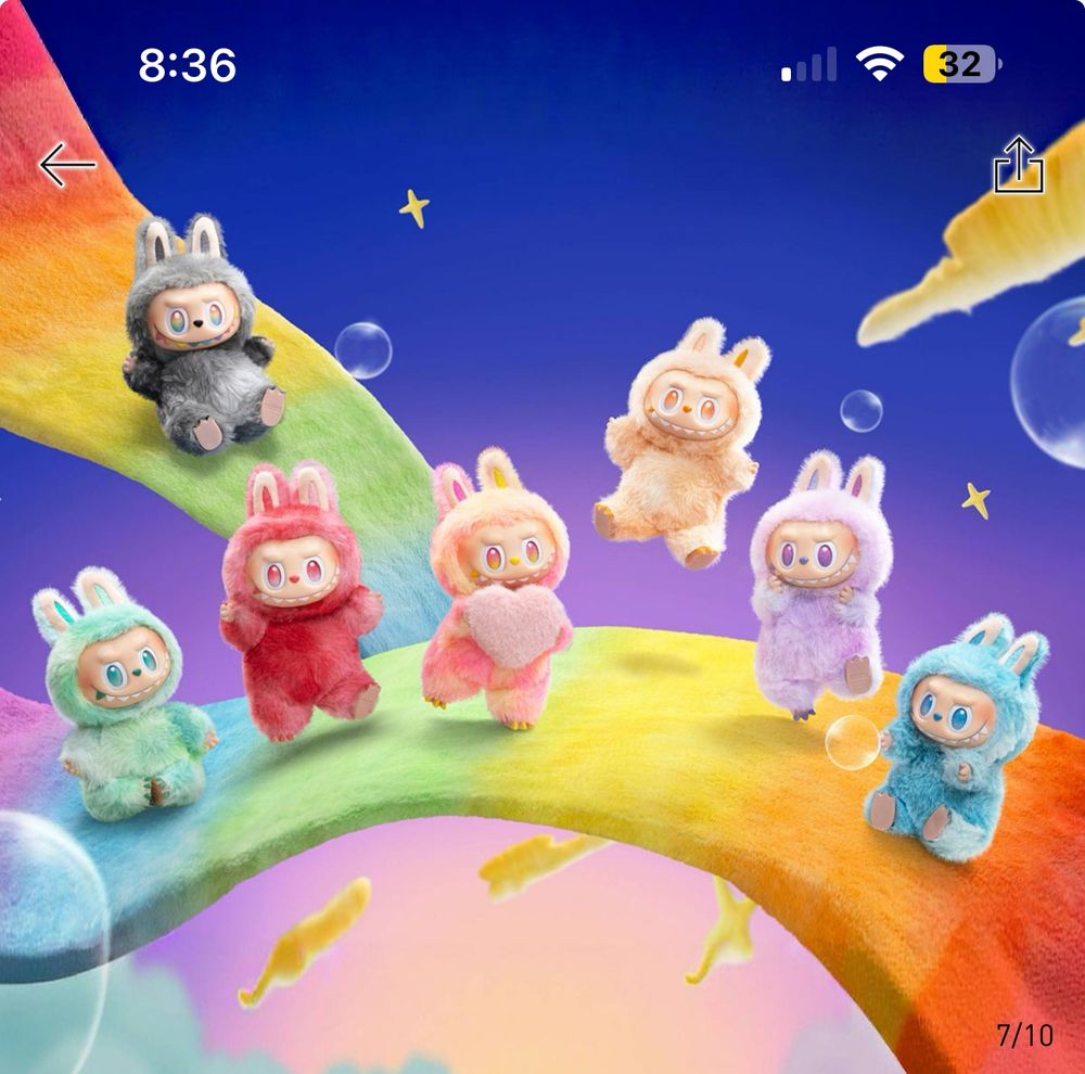 A fantasy scene featuring all the The Monsters’ Big Into Energy plush figures. They sit and stand whimsically. The Monsters’ fur is tie-dyed in various bright  rainbow colors. 