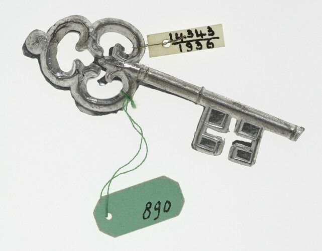 Ornate silver key with green and white labels with handwritten numbers attached.