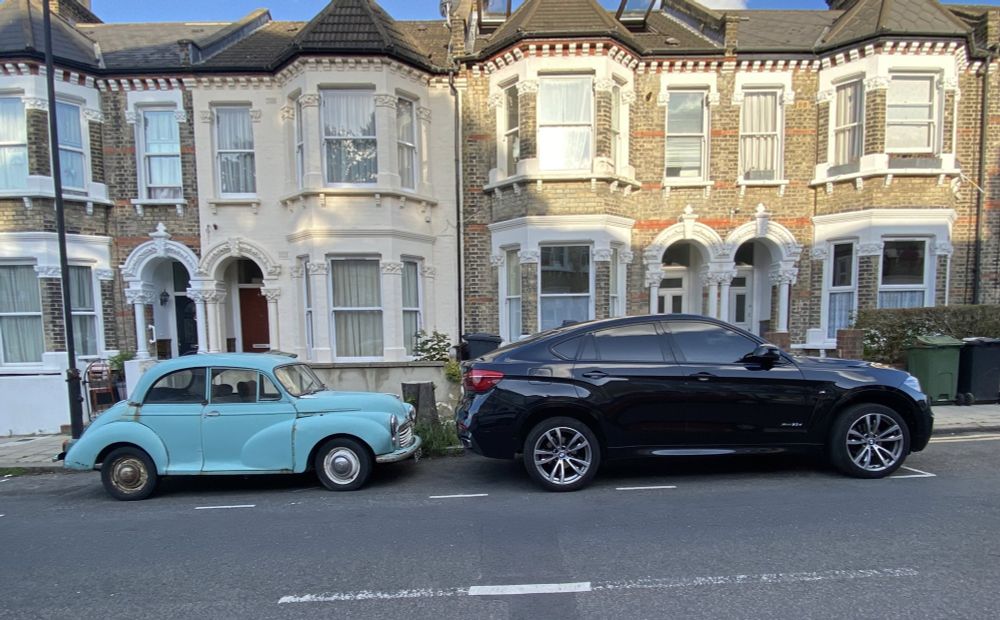 A Morris Minor parked next to a huge new SUV.