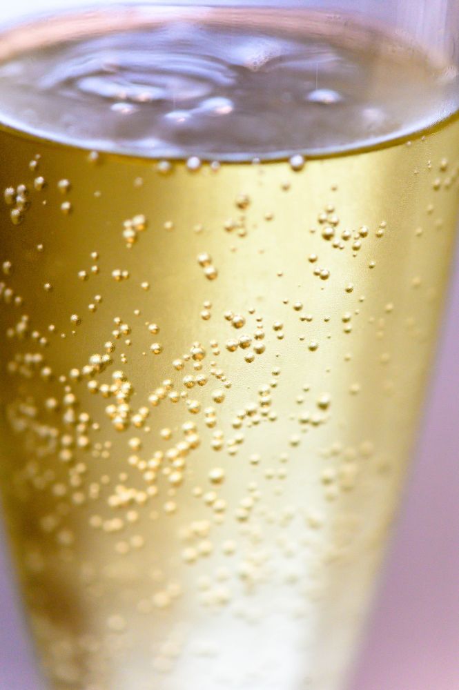 A close-up of a glass of sparkling beverage, featuring golden liquid and numerous small bubbles.