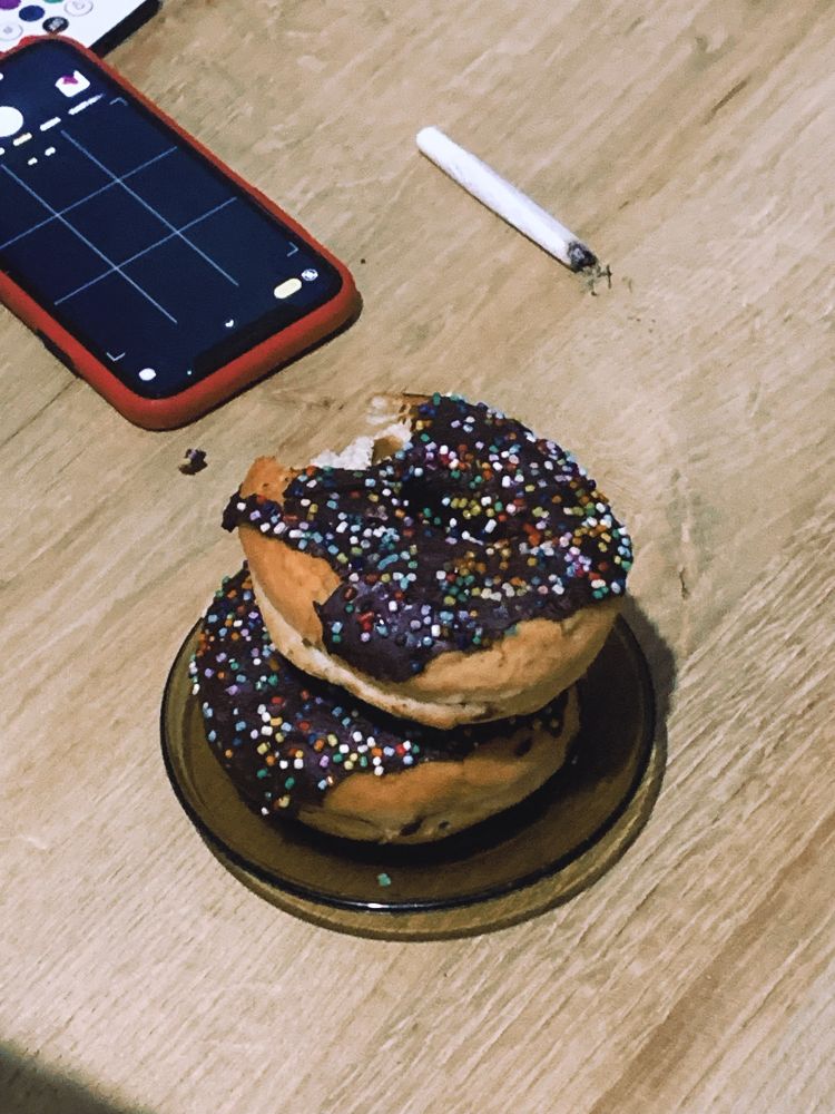 zoomed in picture of the stacked donuts and one of then already got a bite. there is also a phone with a red case and a burnt cigarette 
