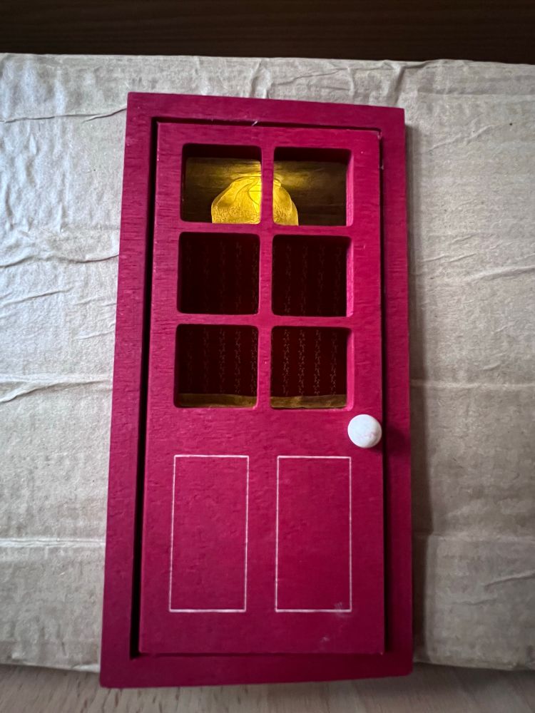 Rote Holztür durch die man eine leuchtende Deckenlampe sieht