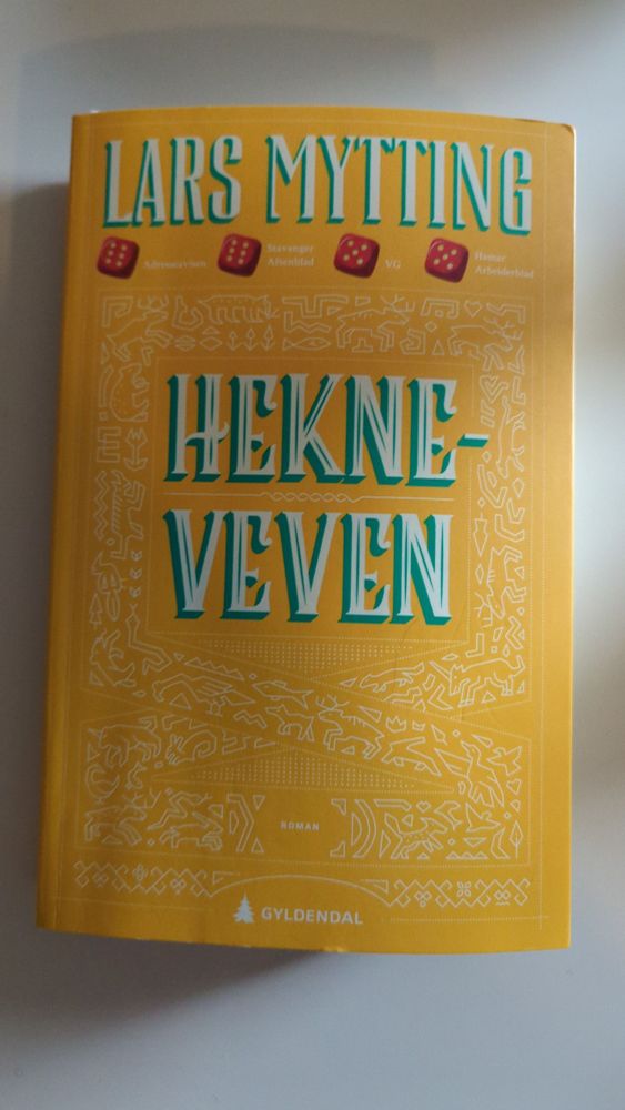 Bilete av boka 'Hekneveven' av Lars Mytting. Boka har gult omslag, med kvit og blå tekst på tittelen. Blåfarga er den same som på omslaget til første bok. Fargar er viktig i boka. I omslaget er det svakt trykt eit mønster av dyr, fuglar og blomar - kanskje veva figurar. 