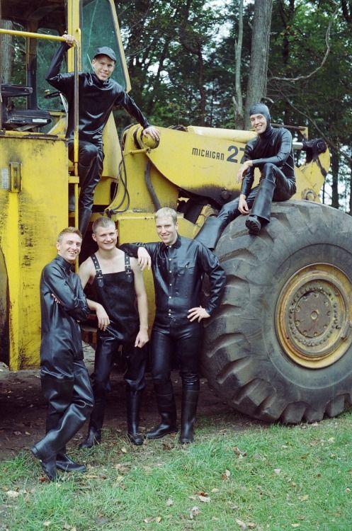 A group of rubber clad young men sitting atop a large tractor. 