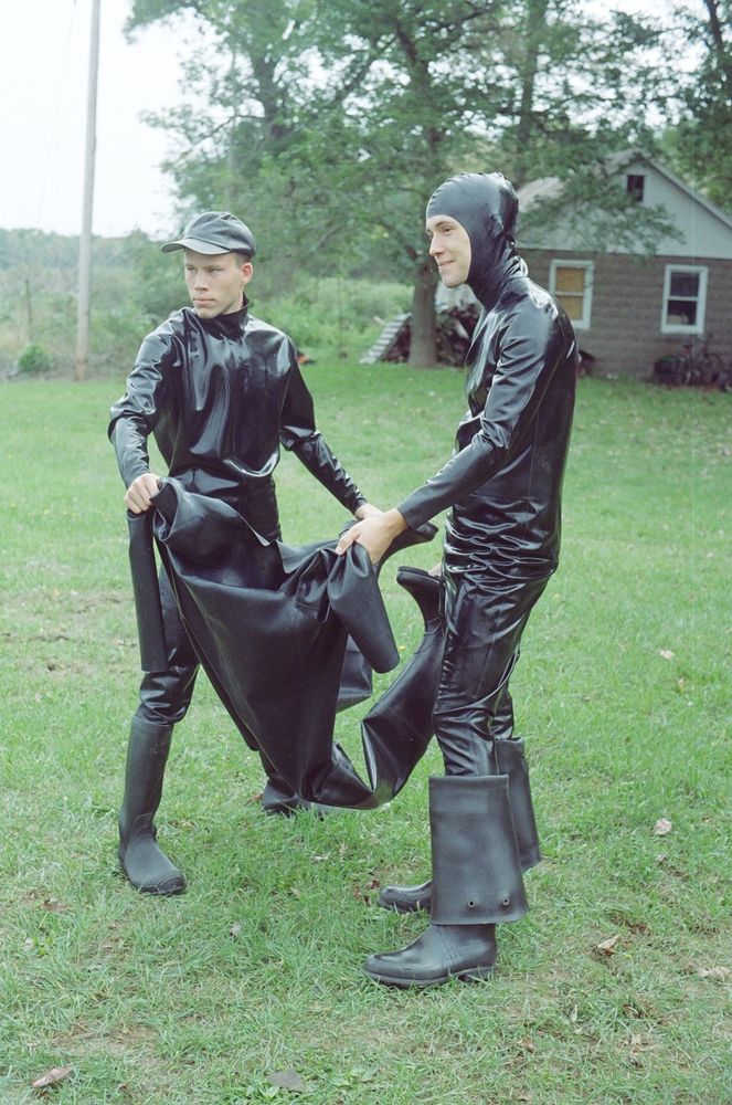 A photo of two latex covered boys holding a heavy rubber suit between them.