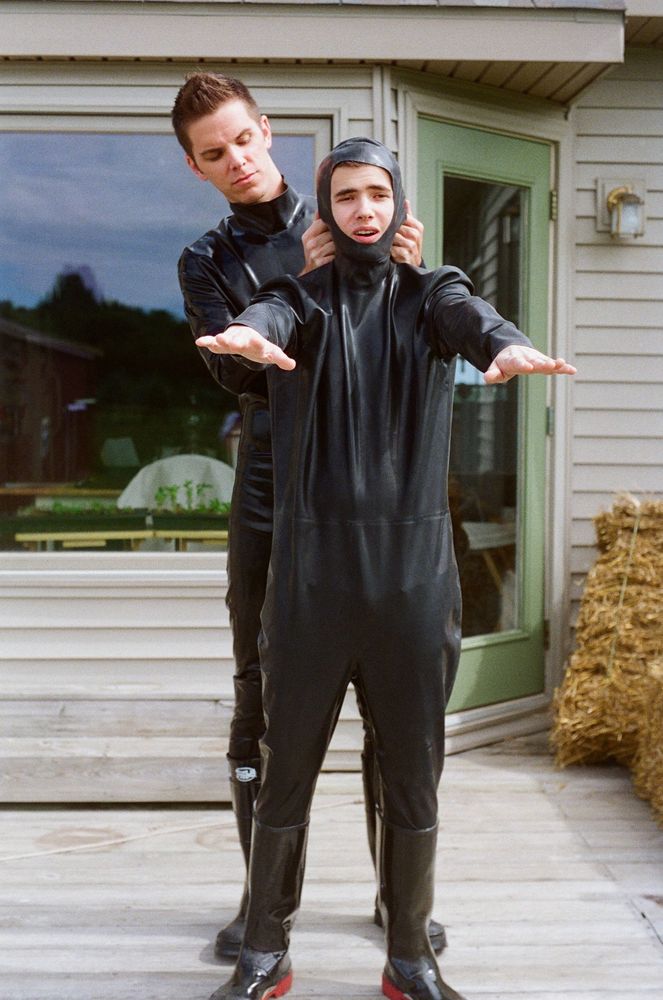 A man is being helped into a rubber suit by a tall rubber boy.