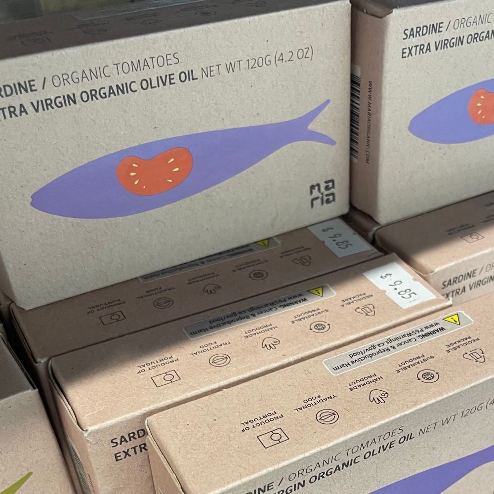a shelf of sardines in fancy illustrated craft paper packaging with a $9.85 price sticker 