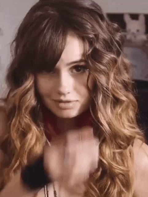 a woman with long curly hair and bangs is wearing a choker necklace .