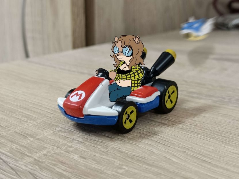 Jamie "driving" Mario's Hot Wheels standard kart, oblivious to a blue shell coming closer towards her.