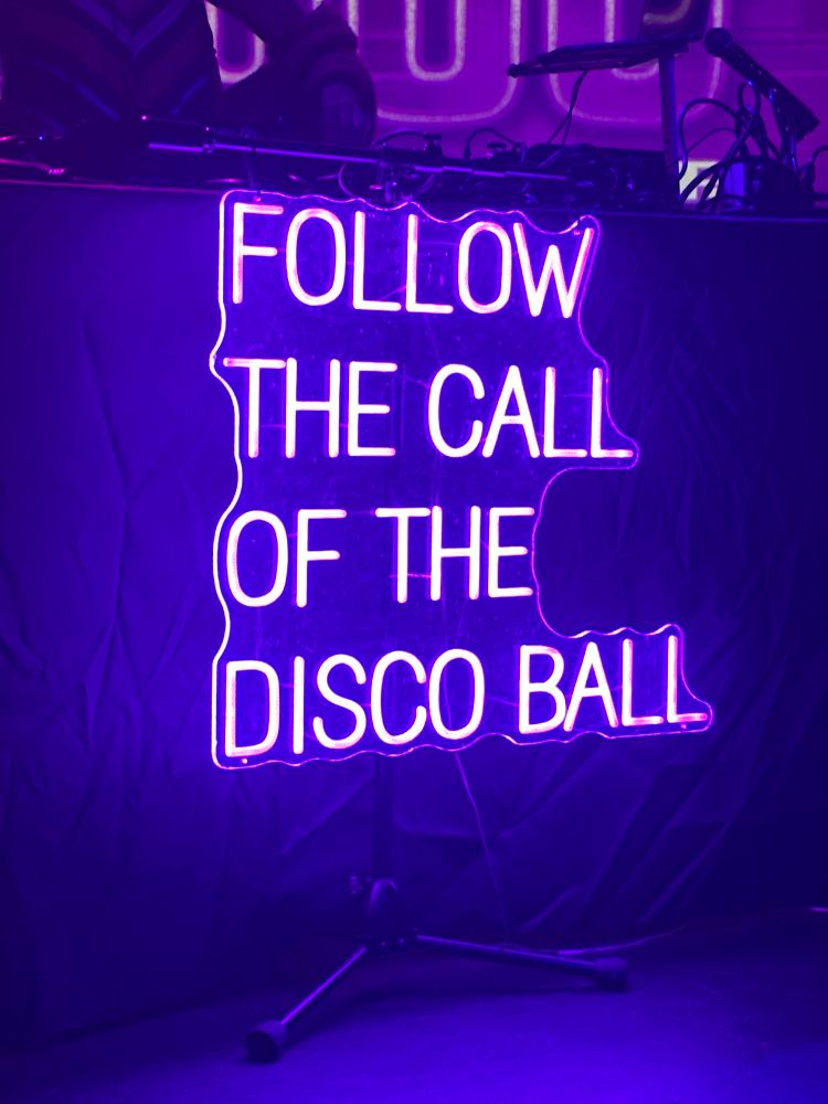 Purple LED sign that says “Follow the call of the disco ball” 