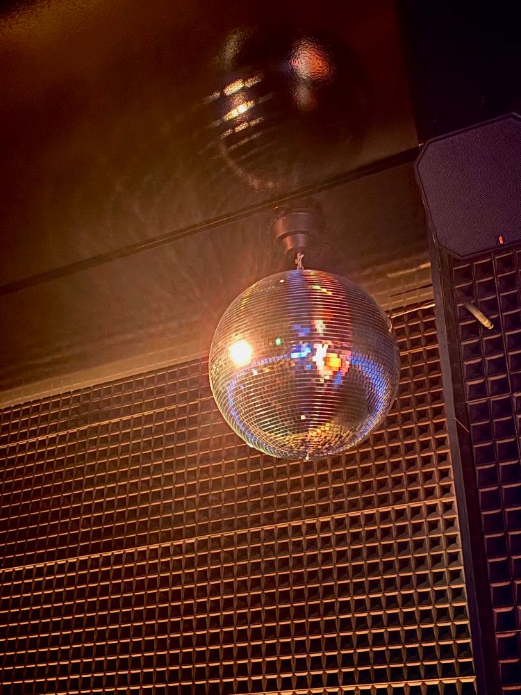 Picture of silver disco ball hanging from ceiling, there is a dark gray square-patterned wall