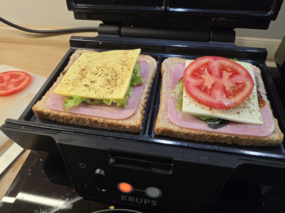 A open sandwich maker with sandwich toast, a slice of ham, lettuce, spiced ketchup, cheese and tomato. 