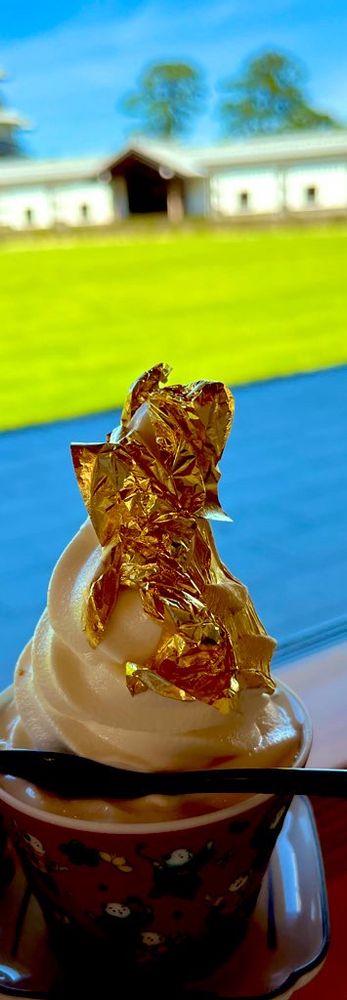金箔を乗せたソフトクリームの画像。背景に庭があり、緑の芝生が生えている。