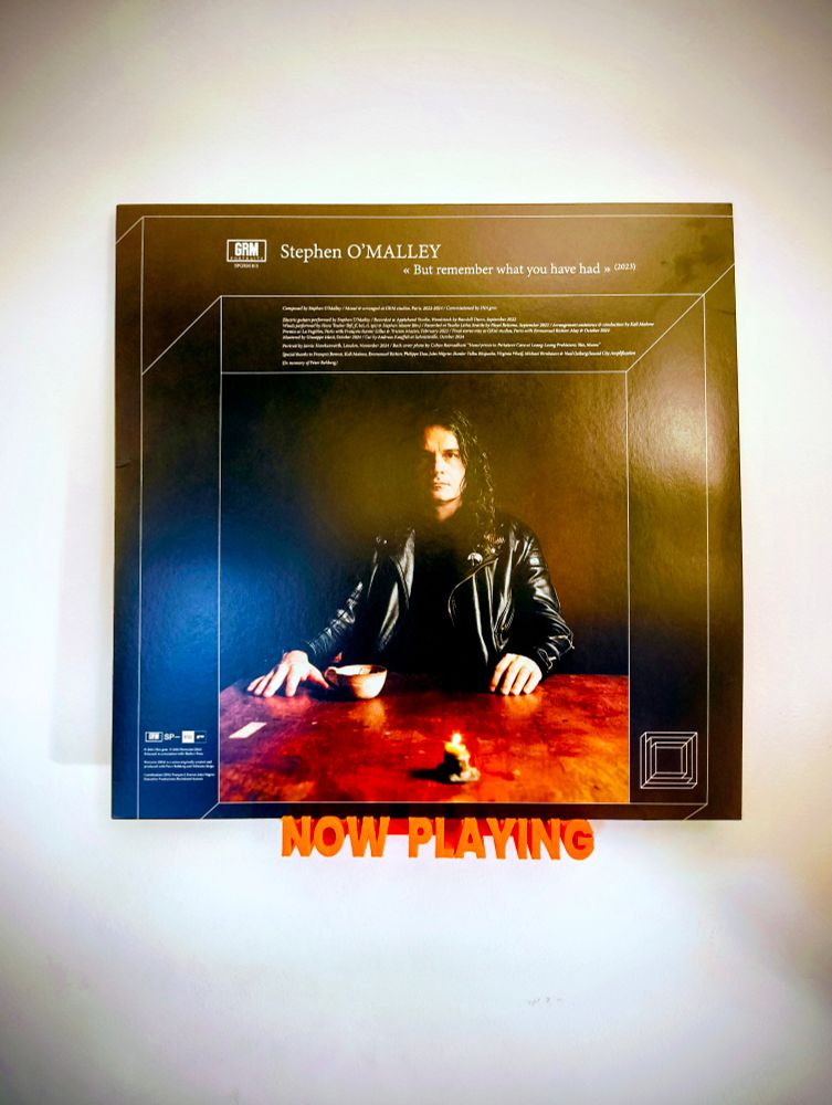 A vinyl copy of Stephen O'Malleys "but remember what you have had" sitting on a small orange shelf in the show of letters spelling out "now playing."