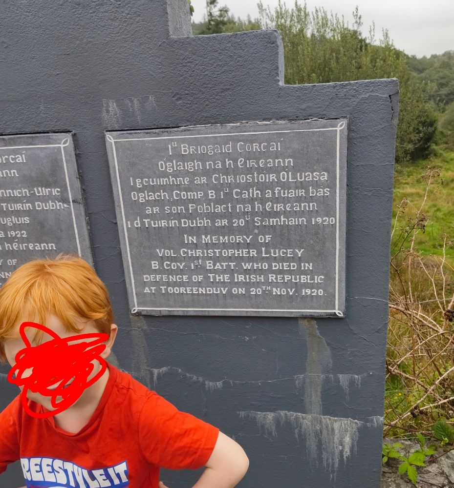 A red haired boy in front of a memorial for a volunteer killed in the Irish war of independence.