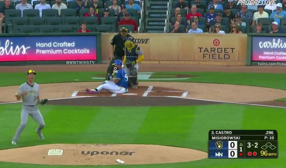 Screen grab of a Brewers pitcher immediately celebrating after a 3-2 pitch. The Twins batter has somehow wound up sitting on home plate, with his head right where the pitch he swung at was. 