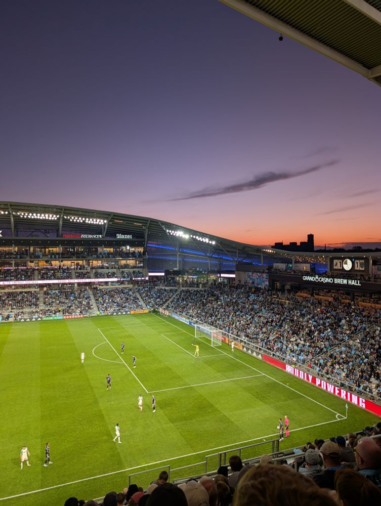 The sun setting over one end of the stadium, some buildings silhouetted in the orange background