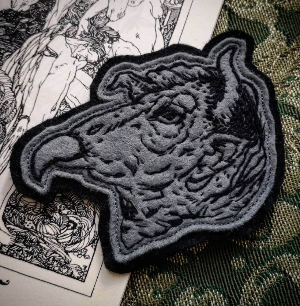 Hand sewn grey felt patch depicting a grotesque vulture-like head with horns in black thread