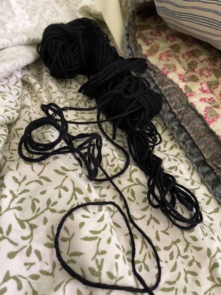 A small tangle of black yarn on bed sheets. 