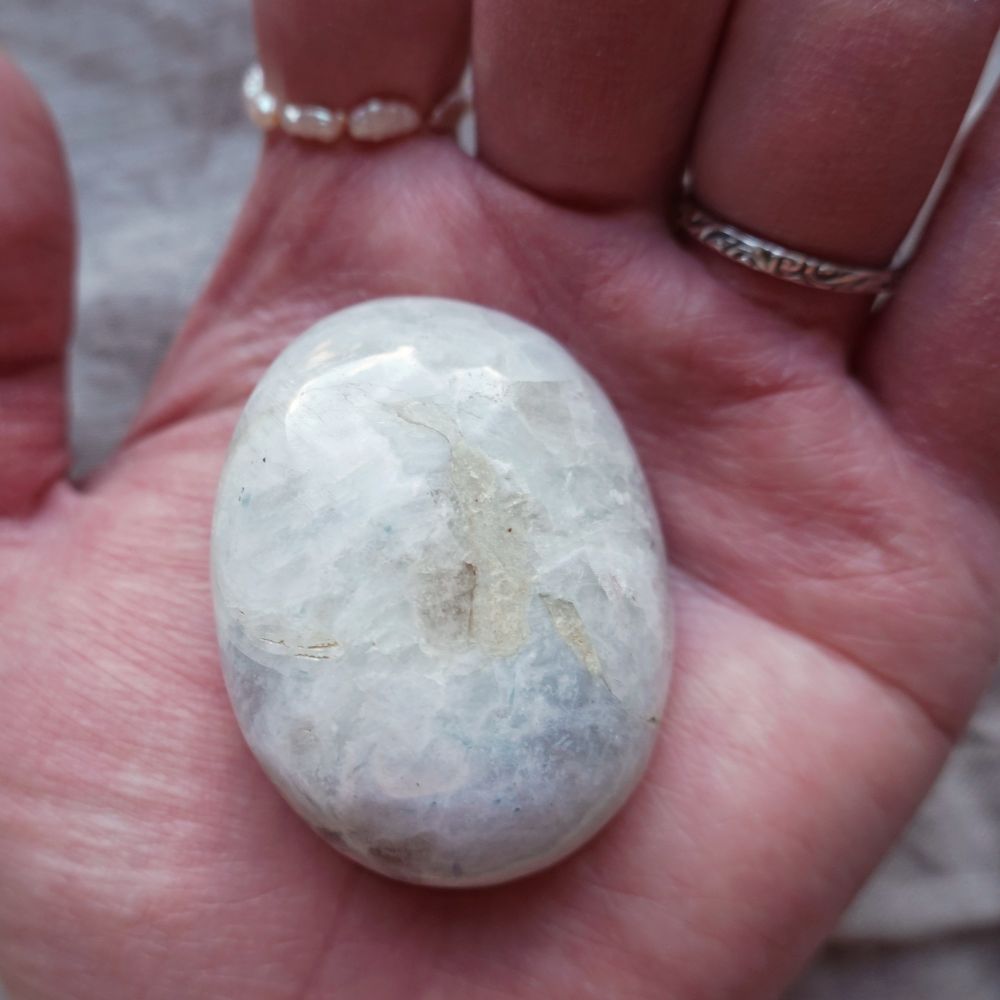a hand wearing two rings holding a moonstone