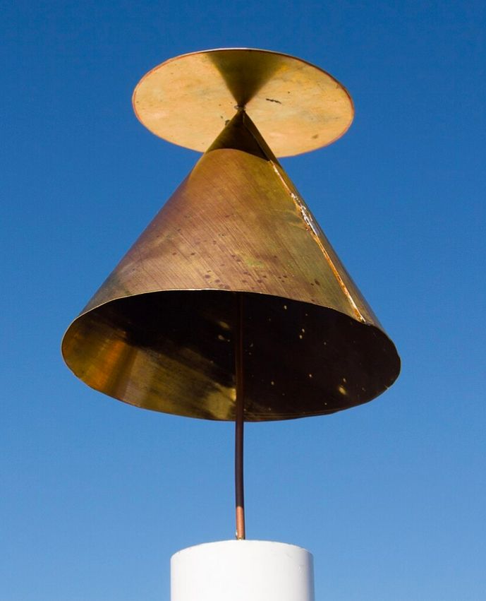 An antenna consisting of a metal disk above a metal cone. The cone points upwards and is made of solid copper. There is a smaller, flat copper disk mounted horizontally, slightly above the tip of the cone. A metal rod extends from the mount through the point of the cone to the center of the disc.