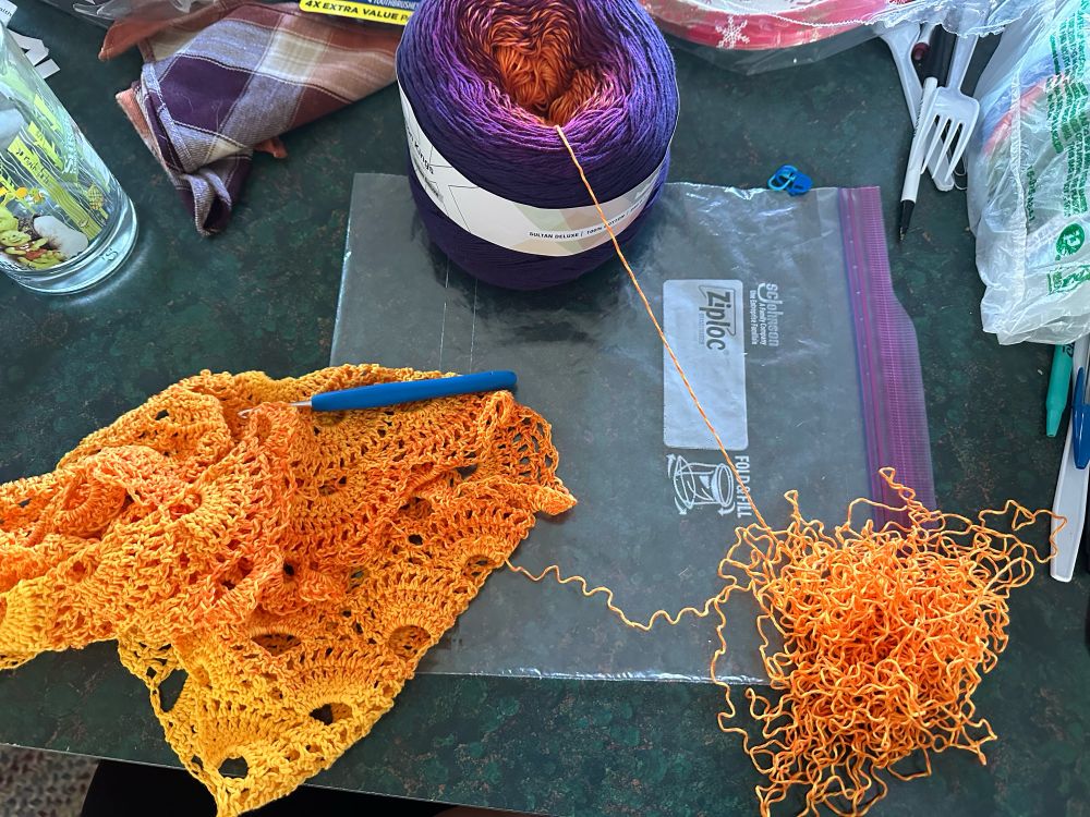 A crochet project on the left side and a pile of yarn on the right that’s been frogged from a mistake. 