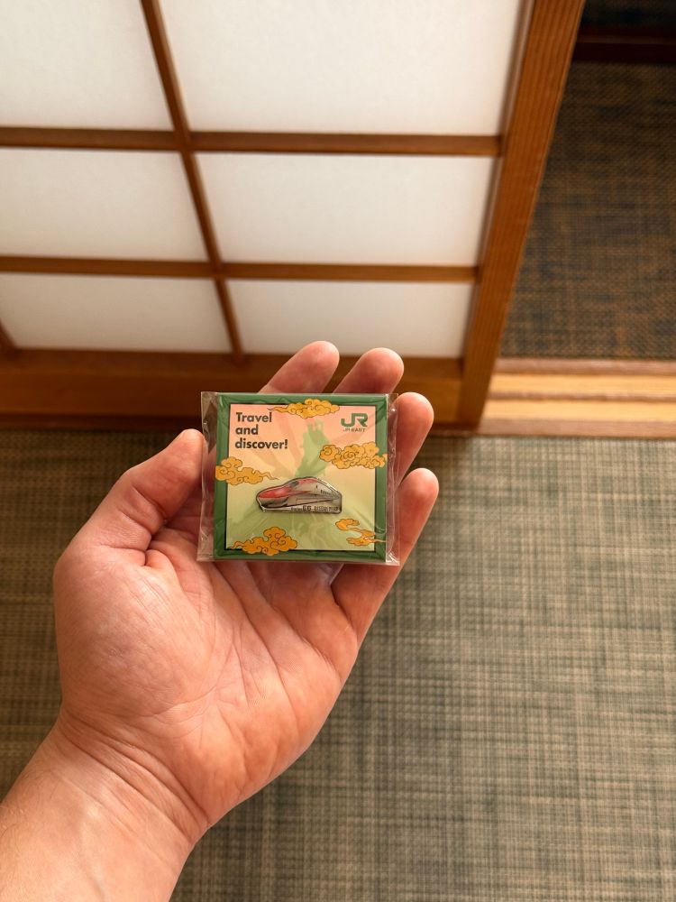 Ein JapanRail East Metallanstecker von einem roten Shinkansen in seiner Verpackung liegt in meiner Hand