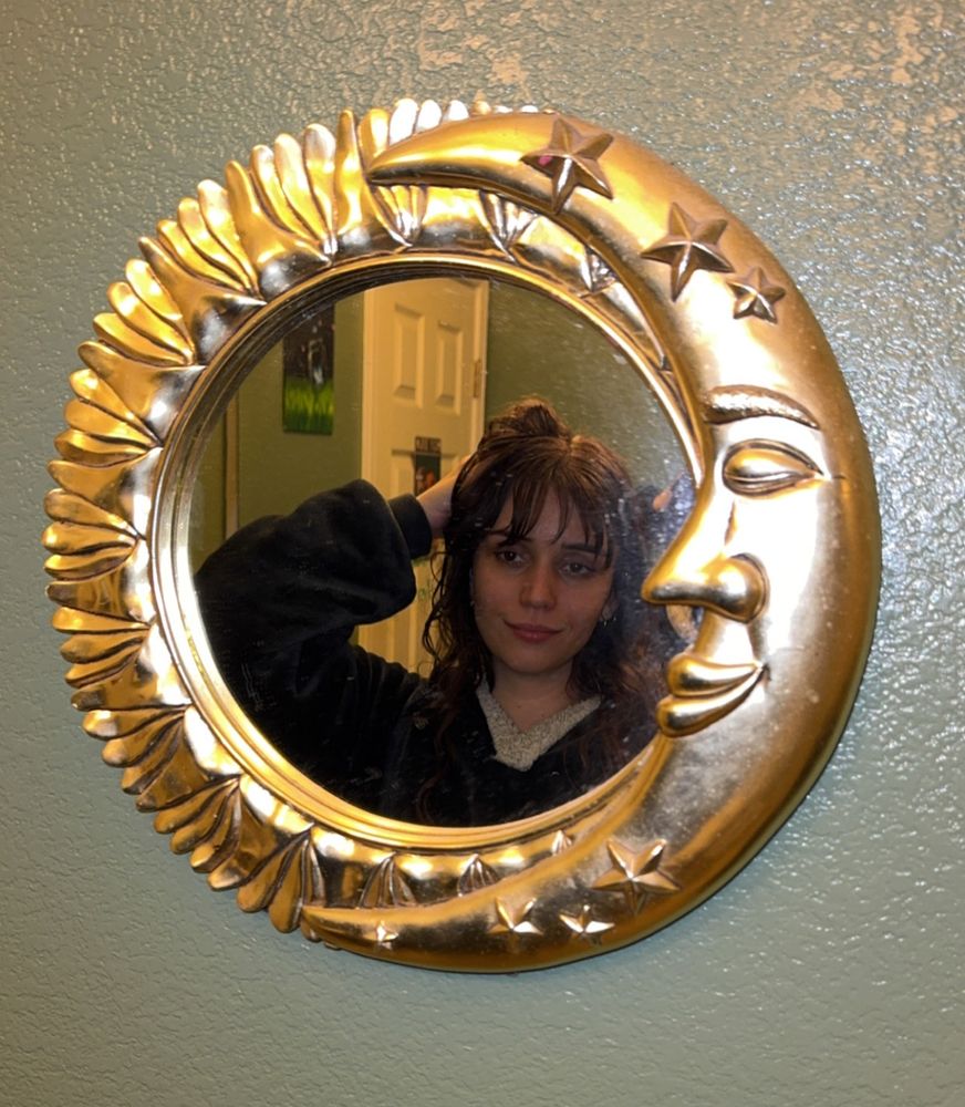 obritwankenobi posing. there is a golden moon mirror on the wall she is using as a prop