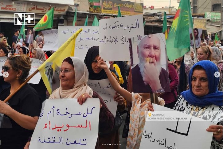 EIne Demonstration mit vielen Frauen. Jemand hält ein Schild des älteren Drusen, dem der Schnurrbart abrasiert wird. Andere halten Schilder mit bspw.


كل صرخة أم يا
 السويداء
تلعن القتلة

bzw. 

"Der Schrei jeder Mutter, oh Sweida, Verdammt seien die Mörder"

Oben links Logo von "N+", unten rechts "Qamishli North Press Agency / Nalin Ali".