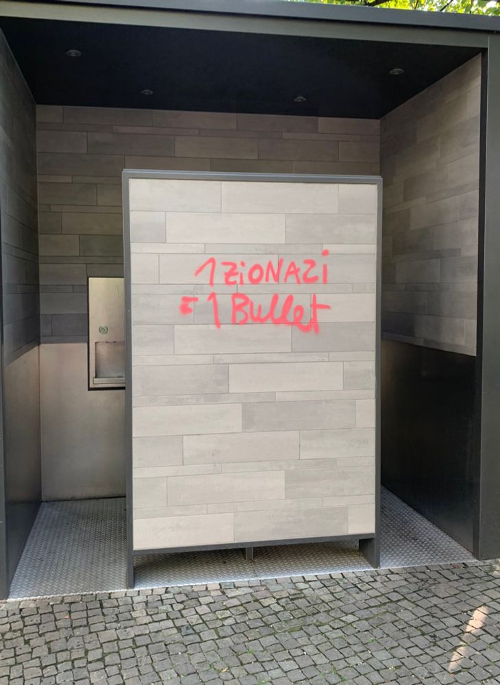 Auf dem mittleren vorderen Teil einer Bezahltoilette wurde in rot "1 Zionazi = 1 Bullet" drauf gesprüht.