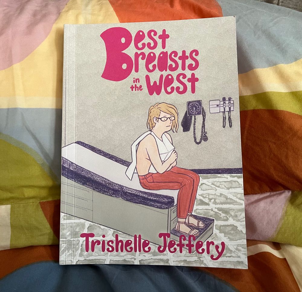 A photo of “Best Breasts in the West,” a graphic memoir by Trishelle Jeffrey. The cover is an illustration of the author sitting on an exam table wearing a flimsy gown.