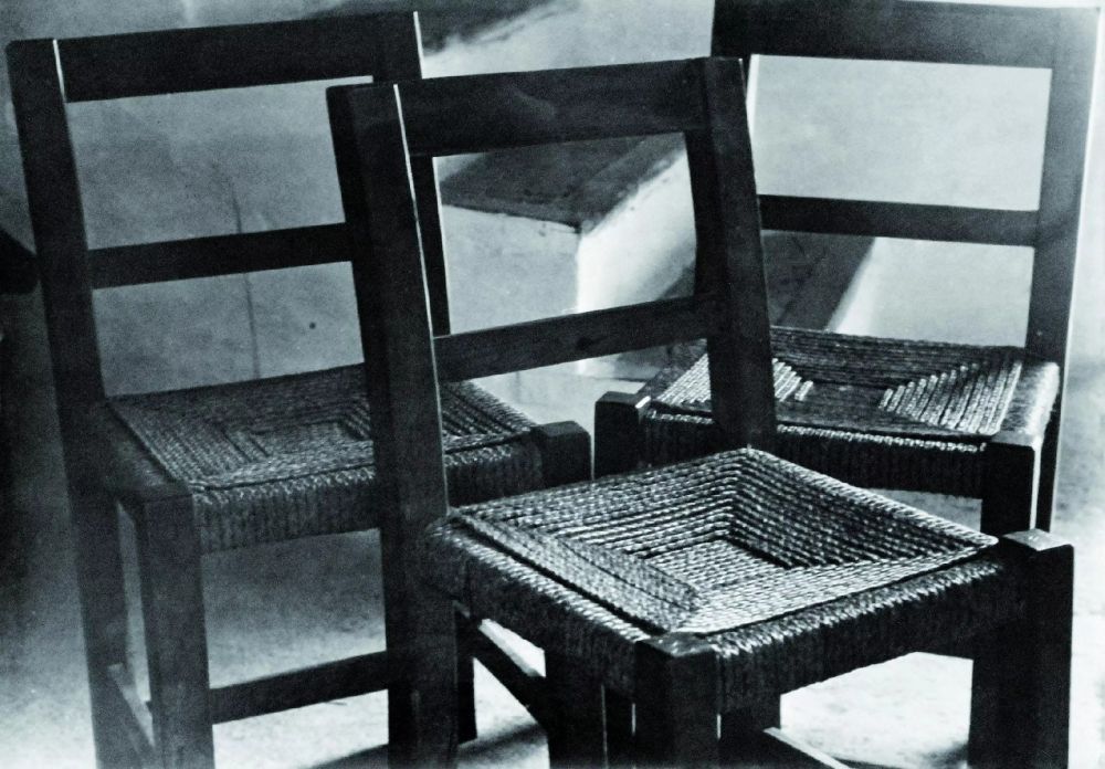 Photographie en noir et blanc de Raoul Haussmann : Trois Chaises, Ibiza 1934. Elles sont en bois et en paille, à la fois simples et avec un travail de la paille particulier, en carrés concentriques. Belle lumière et forts contrastes. On distingue au second plan quelques marches d'un escalier bâti, blanc, typique des intérieurs de fincas et maisons ibicencas. Tout est brut, simple  et d'une beauté saisissante à mes yeux