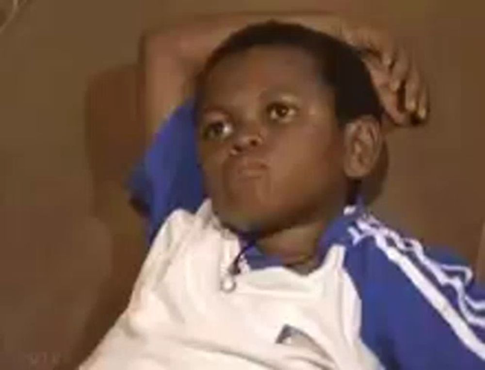 a young boy is sitting on a couch with his hands on his head and making a funny face .