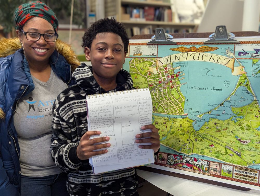 A kid and his mom showing off a notepad with a hand drawn map while standing in front of a colorful map of Nantucket.