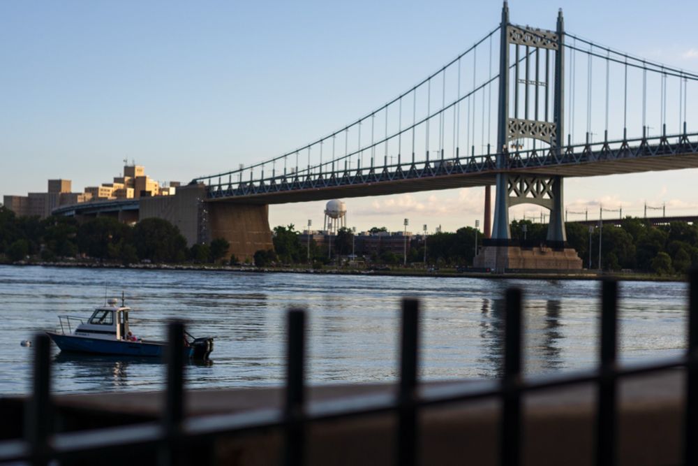 A small boat on the East River. In the background, one of the Triboro Bridge towers 