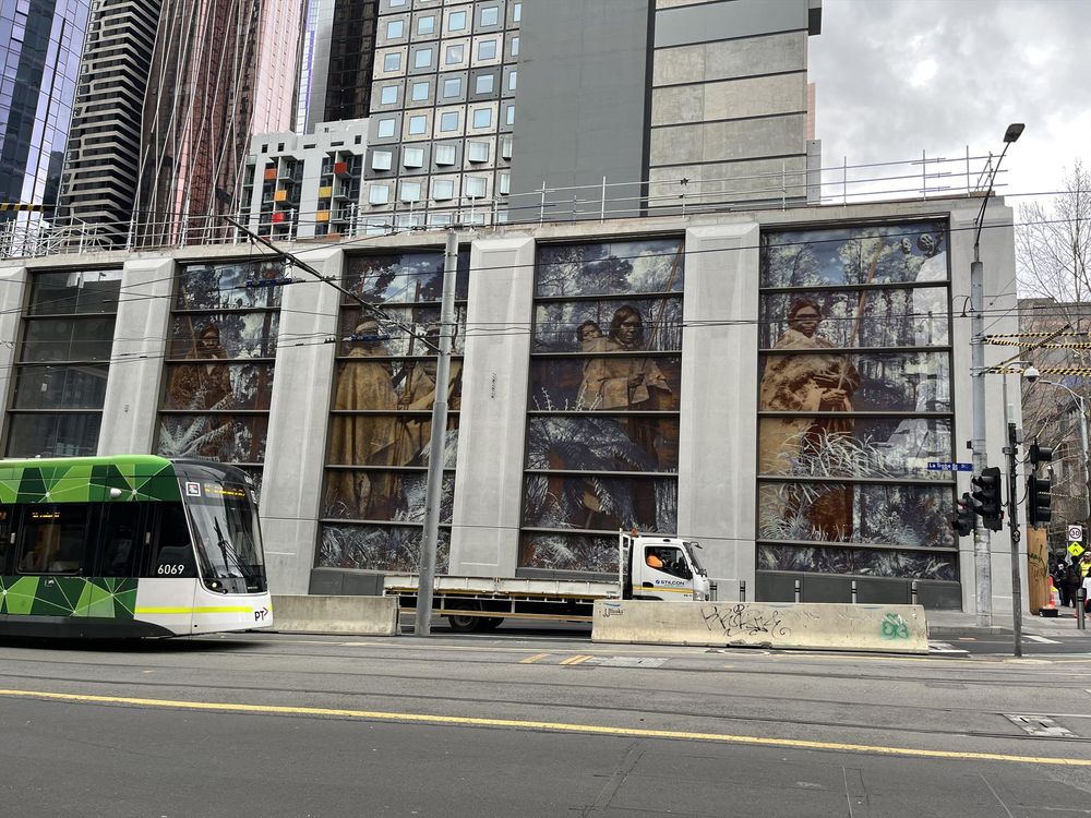 A tram passes a building with a large mural showing First Nations Australians