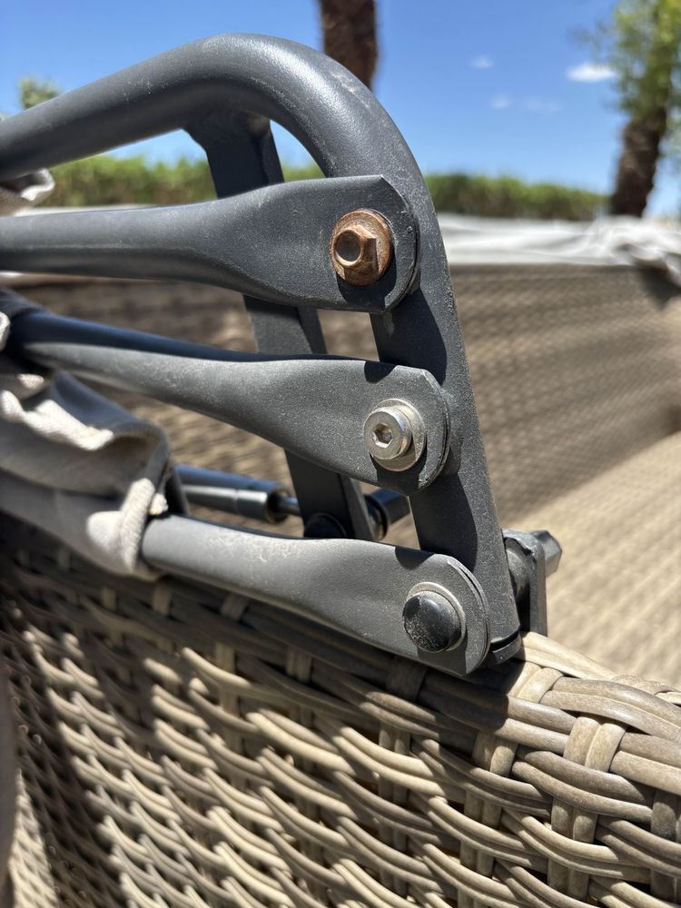 Three parallel steel arms (an outdoor couch's folding sunshade) are attached to a steel support bar with bolts and washers. One is rusted and brown.