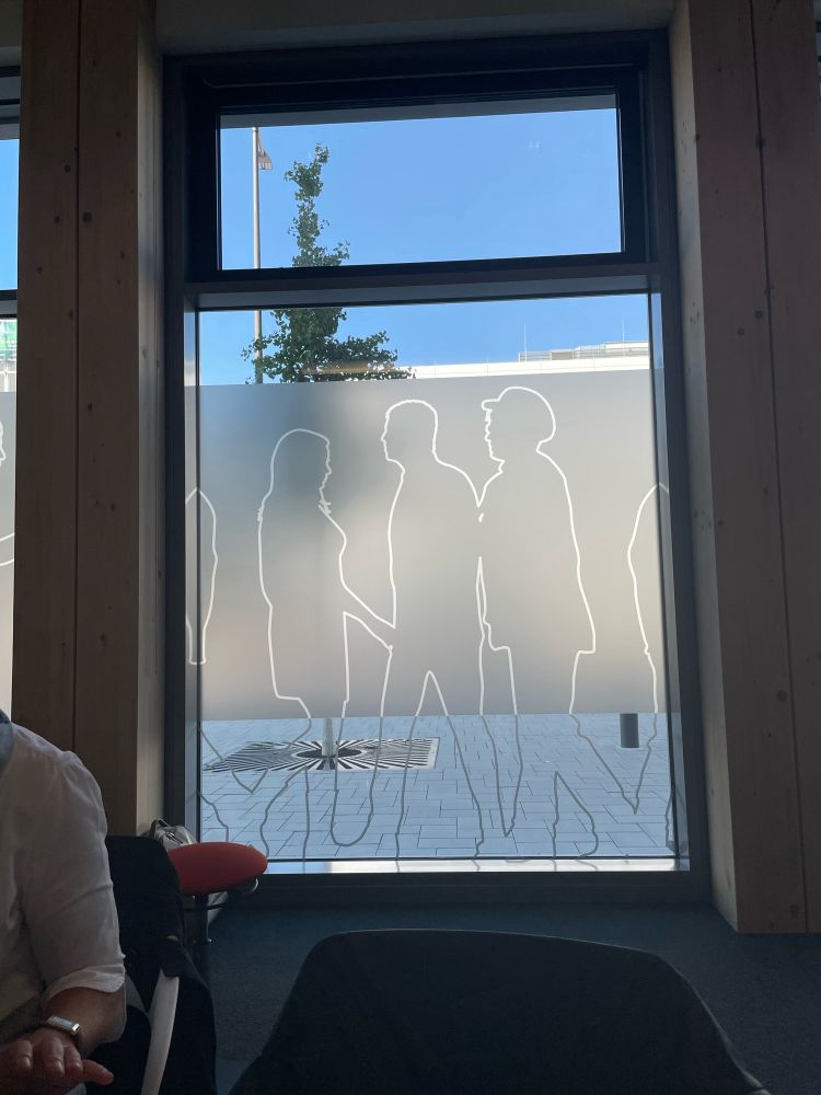 Fenster mit Folie, bei der Silhouetten von Menschen zu sehen sind. Es sieht so aus als ob eine Frau einem Mann in den Schritt greift.