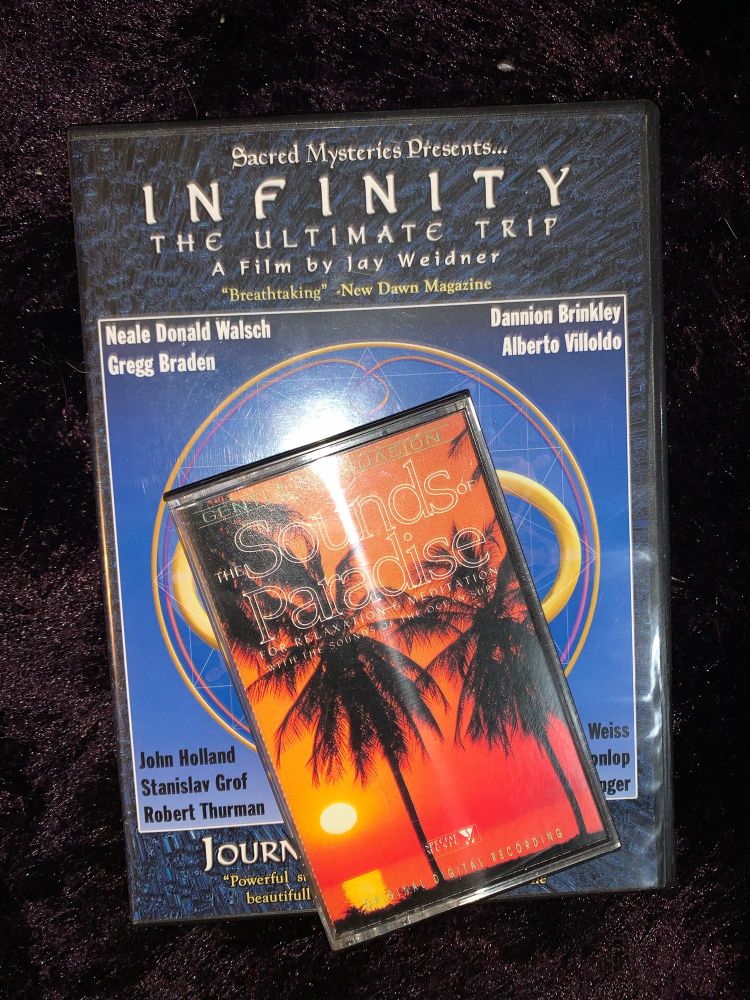 A flash phone picture of an esoteric dvd laying on a purple shag carpet. The dvd cover design has a blue grey color palette and sitting on top is a cassette tape with palm tree silhouettes and deep shades of reds and oranges. The flash from the phone camera is reflecting off of all the surfaces.