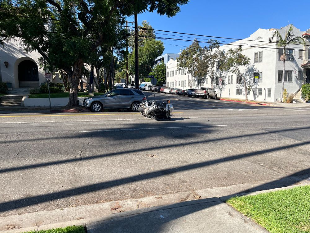 A damaged motorcycle on its side in the middle of the street with noone around.