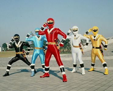 From left to right, the Black Ranger, Blue Ranger, Red Ranger, White Ranger, and Yellow Ranger from "Mighty Morphin Alien Rangers" (1996) posing in a city.