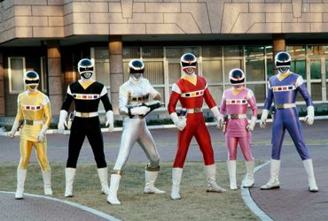 From left to right, the Yellow Ranger, Black Ranger, Silver Ranger, Red Ranger, Pink Ranger, and Blue Ranger from "Power Rangers in Space" (1998) standing behind a building.