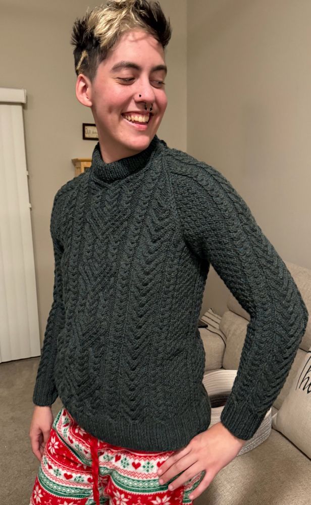 Person modeling hand knit cabled sweater in a living room 