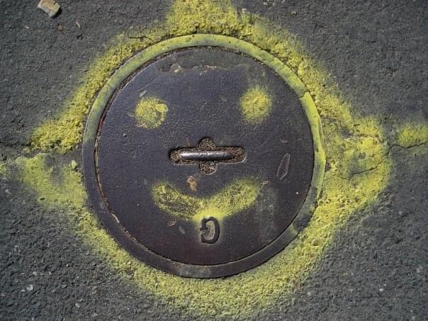 A manhole cover in Portland, Oregon outlined with yellow spraypaint to create ears. A smile and eyes also added.