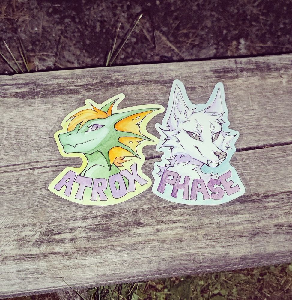 Watercolor basges of a green dragon with orange frills and hair, and a ghost fox, made by Neotheta. 