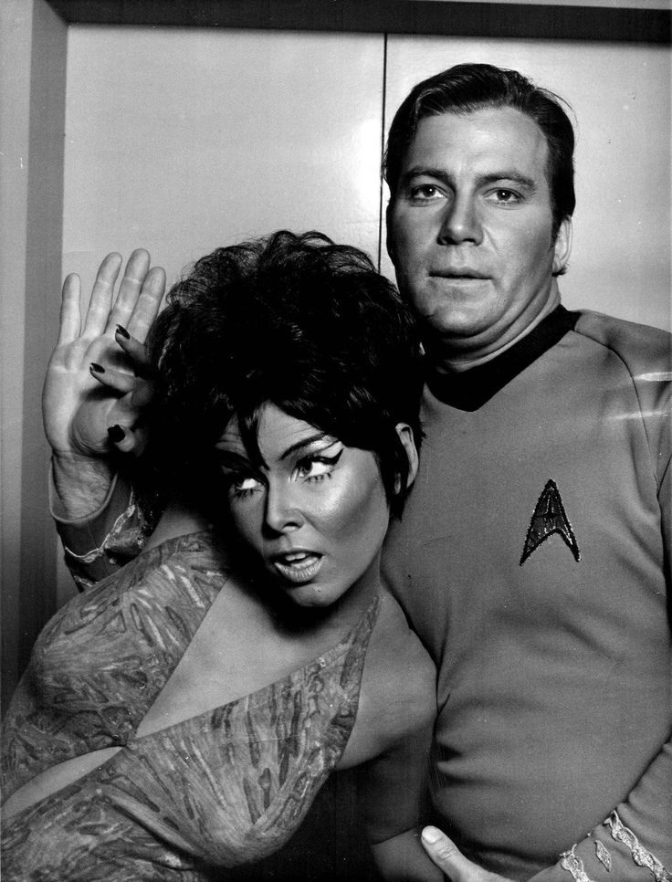 A black & white photo from the original series of Star Trek. Captain Kirk seems to be having a difficult time with an alien...maybe trying to teach her a new dance move. (Actors Yvonne Craig and William Shatner pictured)