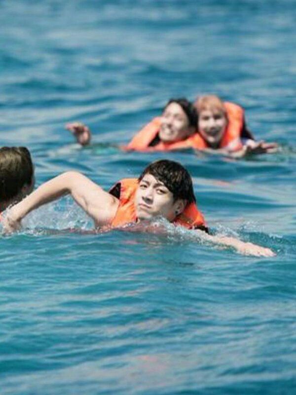 Jungkook is swimming hard in the foreground of the picture while Suga and j-hope appear to be floundering behind him